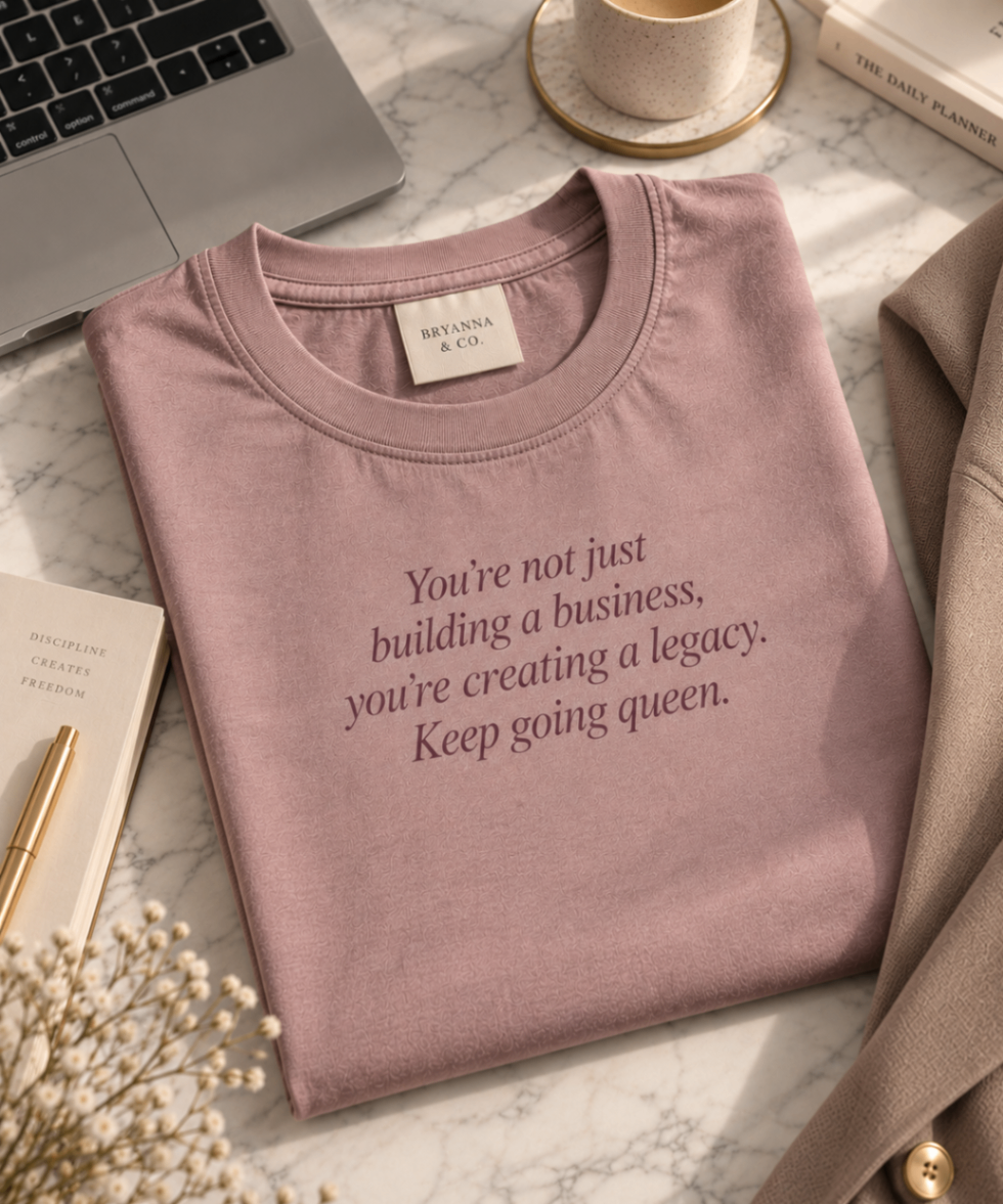 Dusty Mauve relaxed-fit tee printed with “You're not just building a business, you're creating a legacy. Keep going queen.” in mauve serif type, folded on a linen backdrop